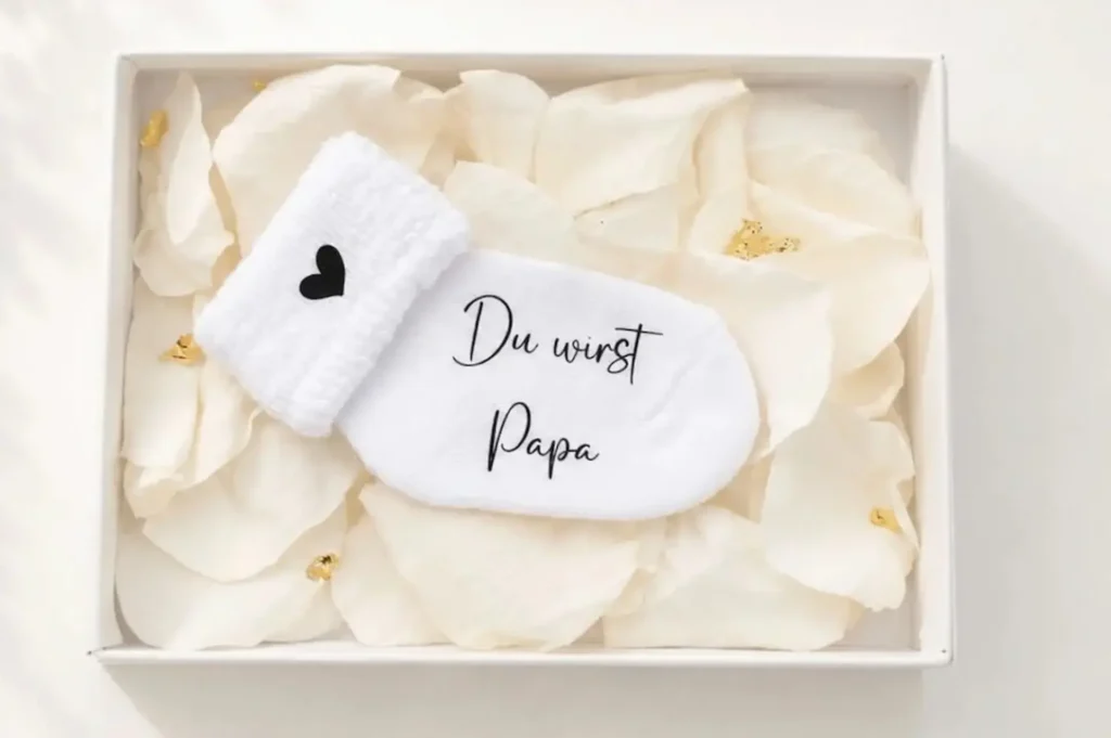 Personalisierte Schwangerschaftsverkündungssocke in eleganter Geschenkbox mit Rosenblättern und Blattgold – liebevolles und einzigartiges Babyankündigungs-Geschenk