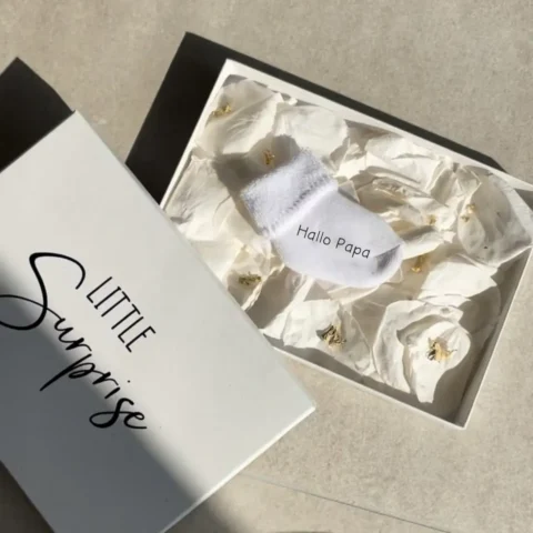 Personalisierte Schwangerschaftsverkündungssocke in eleganter Geschenkbox mit Rosenblättern und Blattgold – liebevolles und einzigartiges Babyankündigungs-Geschenk