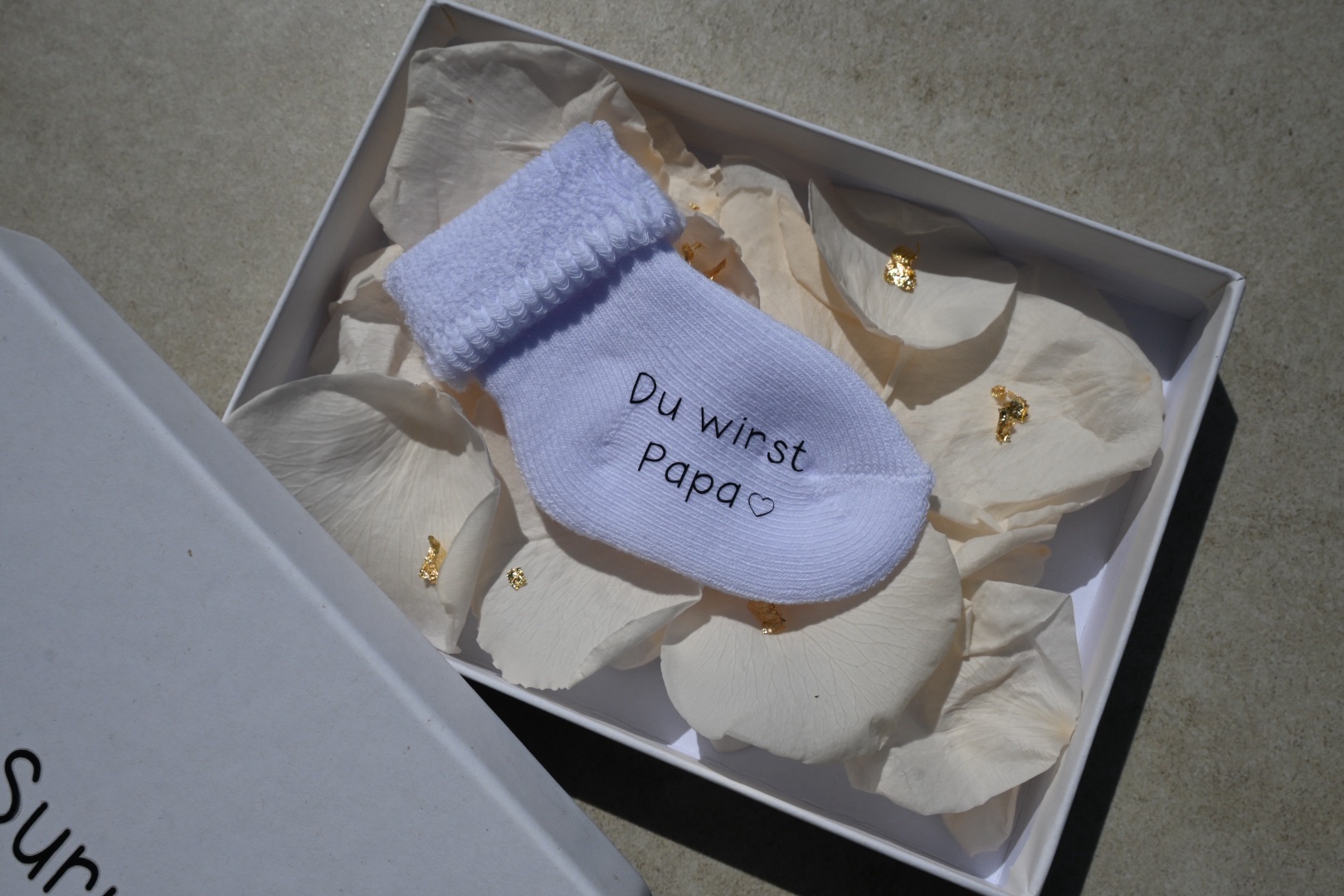 Personalisierte Schwangerschaftsverkündungssocke in eleganter Geschenkbox mit Rosenblättern und Blattgold – liebevolles und einzigartiges Babyankündigungs-Geschenk